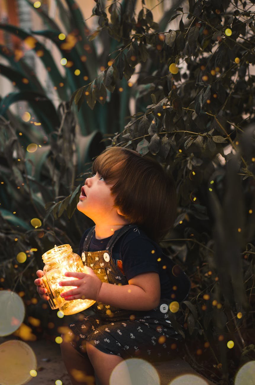 pexels-photo-2026960-2026960 A young child gazes in wonder while holding a jar of lights in a magical forest setting, capturing innocence and curiosity.